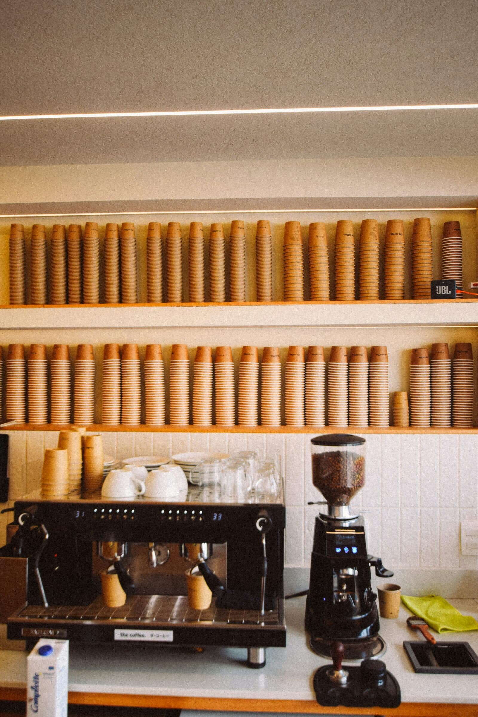 A coffee counter with stacked kraft cups on shelves and an espresso machine.