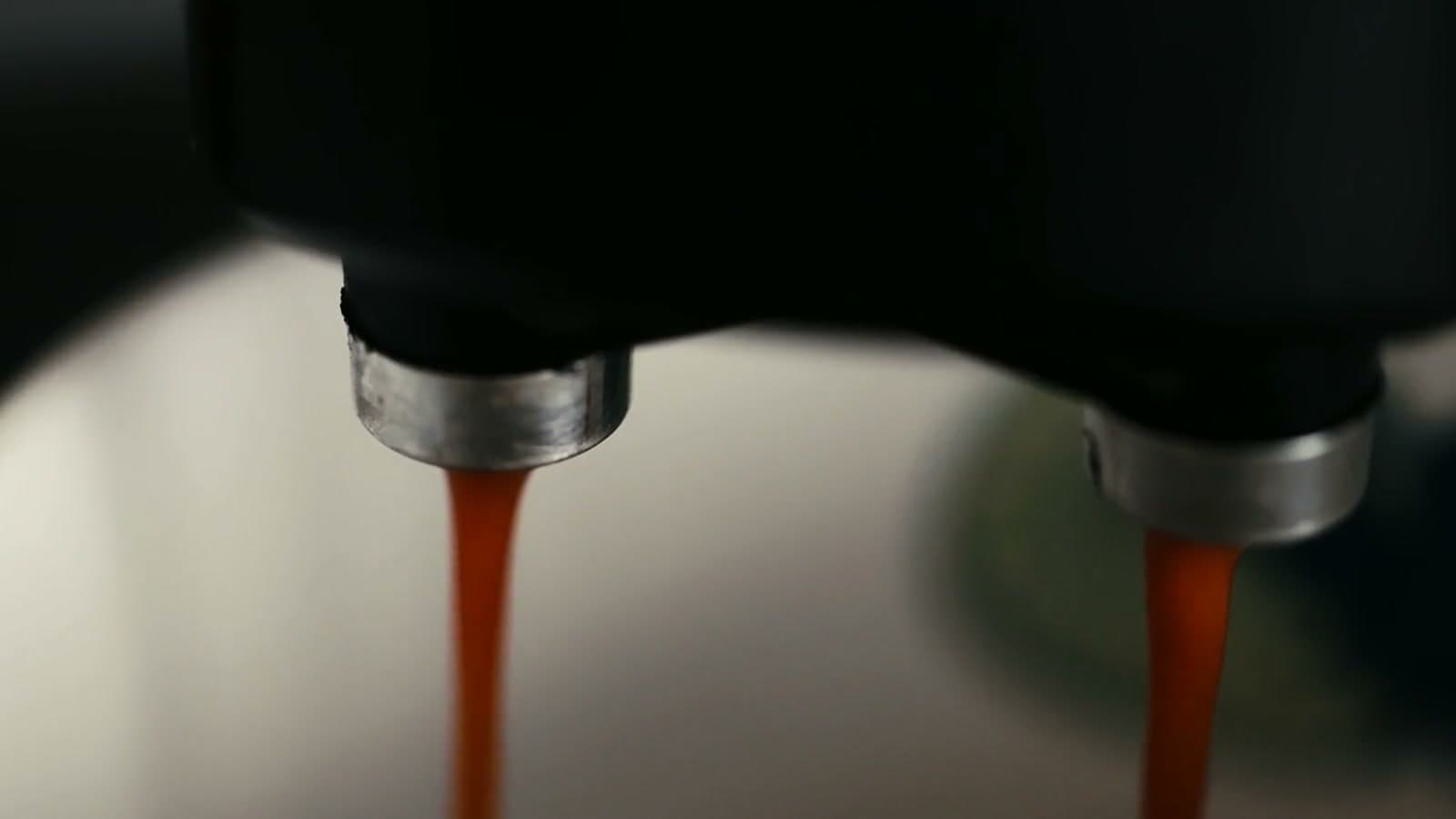 Two streams of espresso pouring from the spouts of a machine.