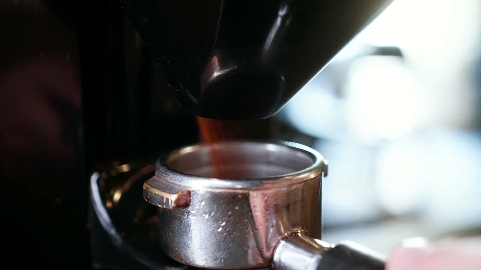 Fresh coffee grounds falling from a grinder into a portafilter.