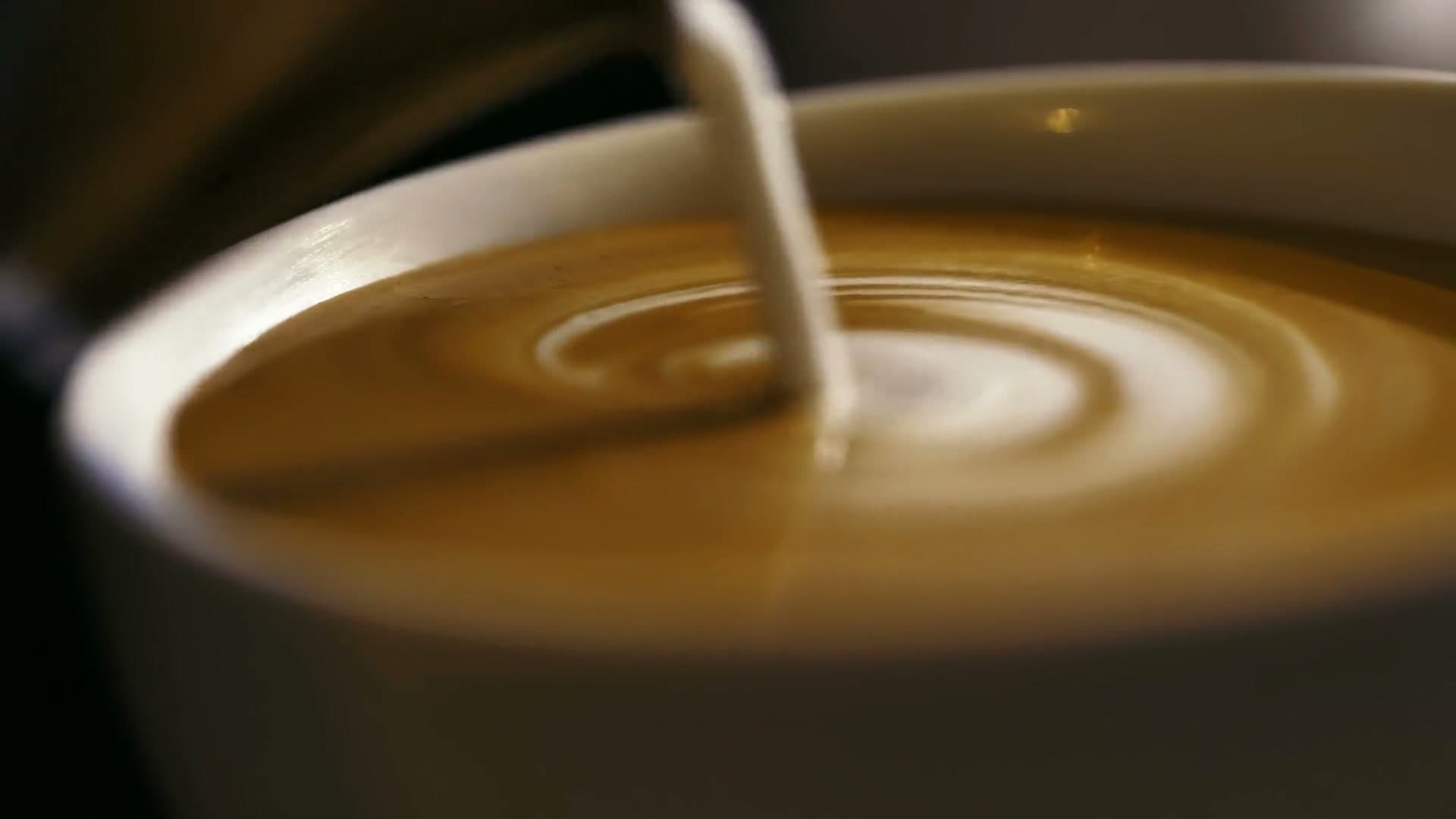A shot of espresso pouring, milk folding into a latte, and a finished latte in a green cup set down on the counter.