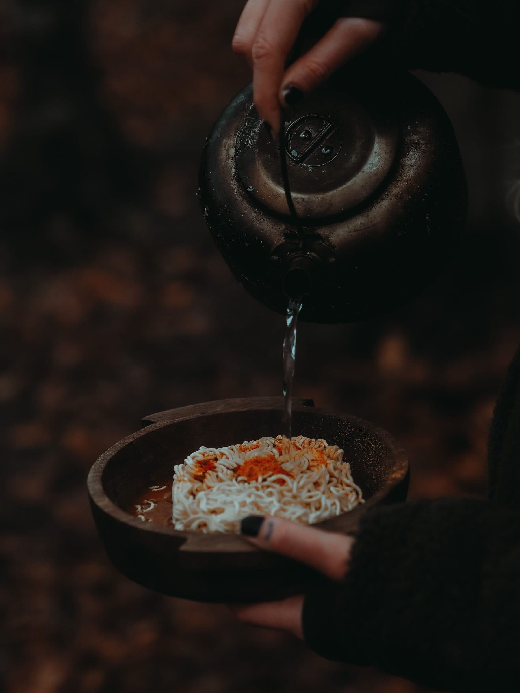 Hot water poured from a kettle over a block of noodles.