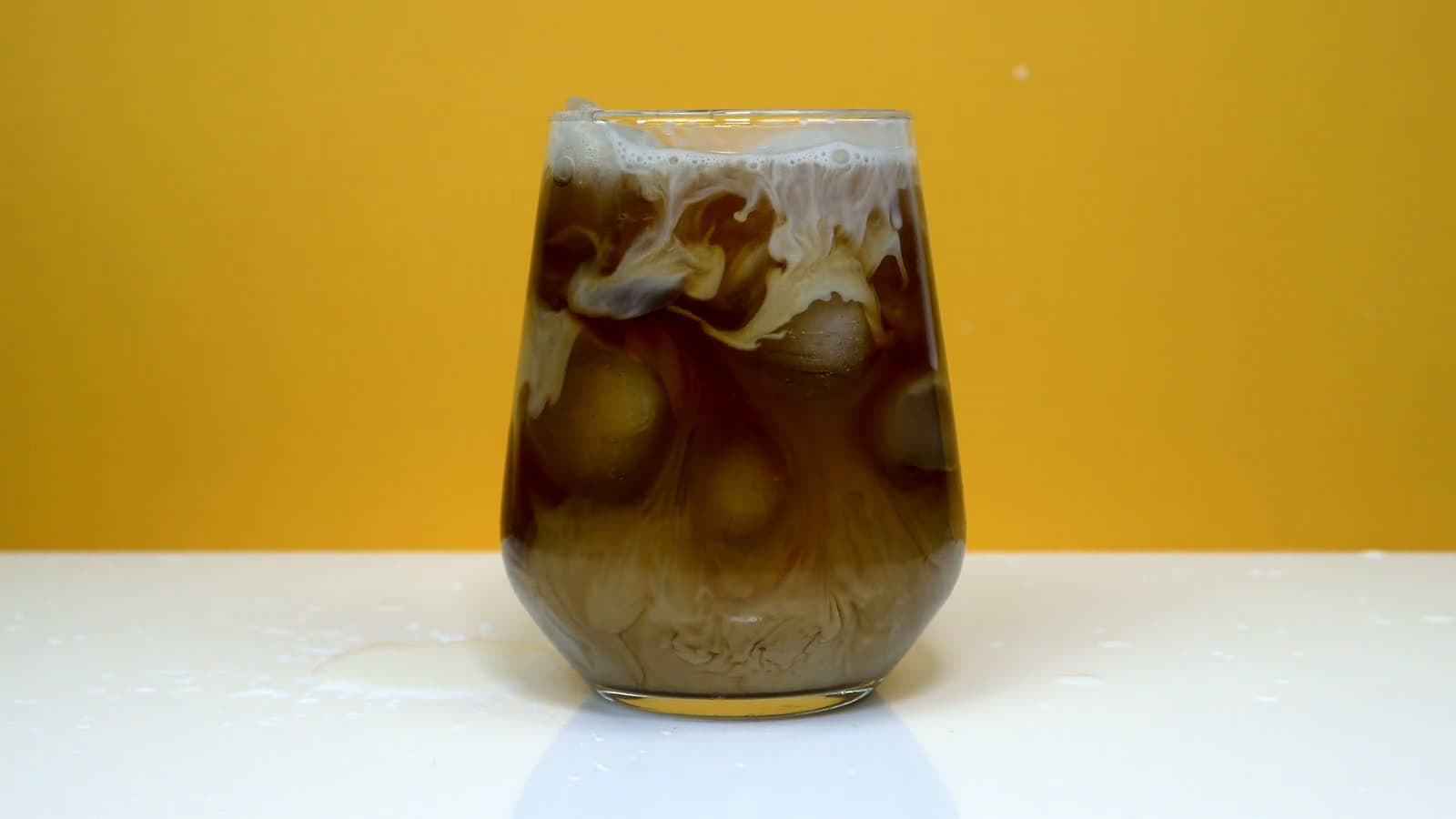 Milk swirls down through ice into a glass of cold coffee.