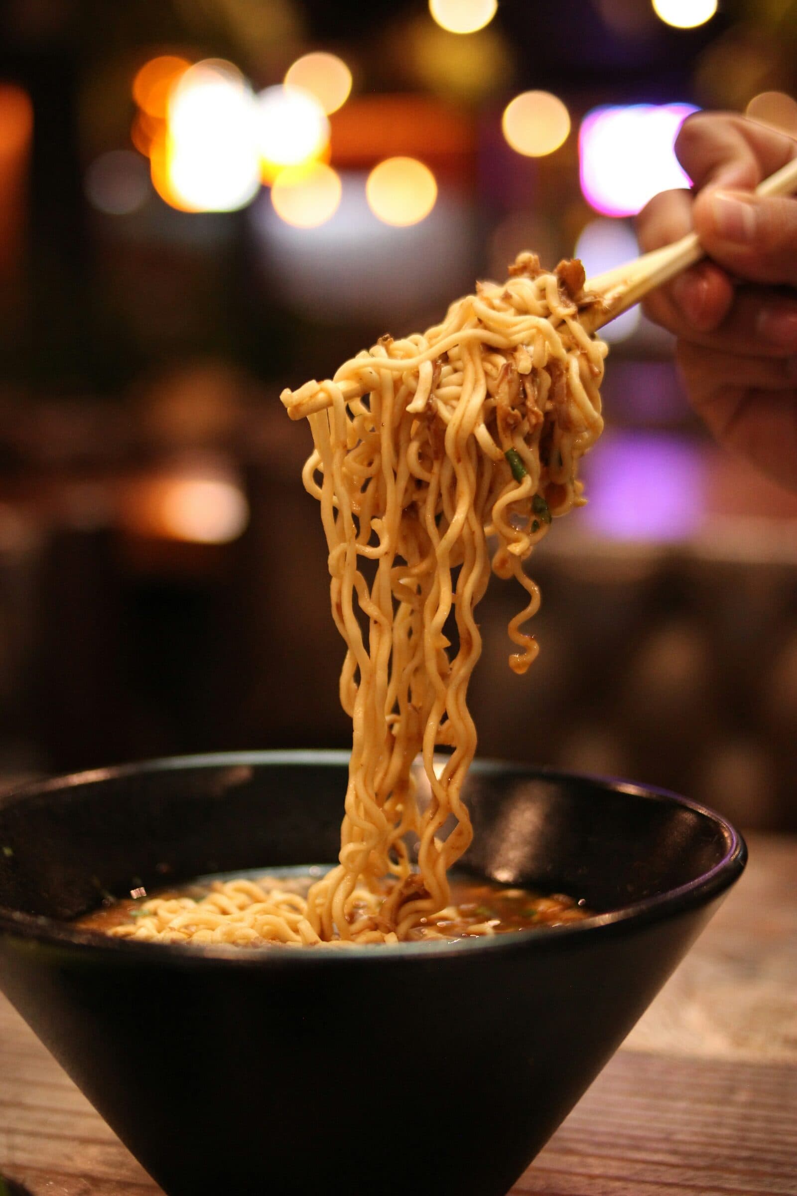 Wavy noodles lifted from a bowl with chopsticks.