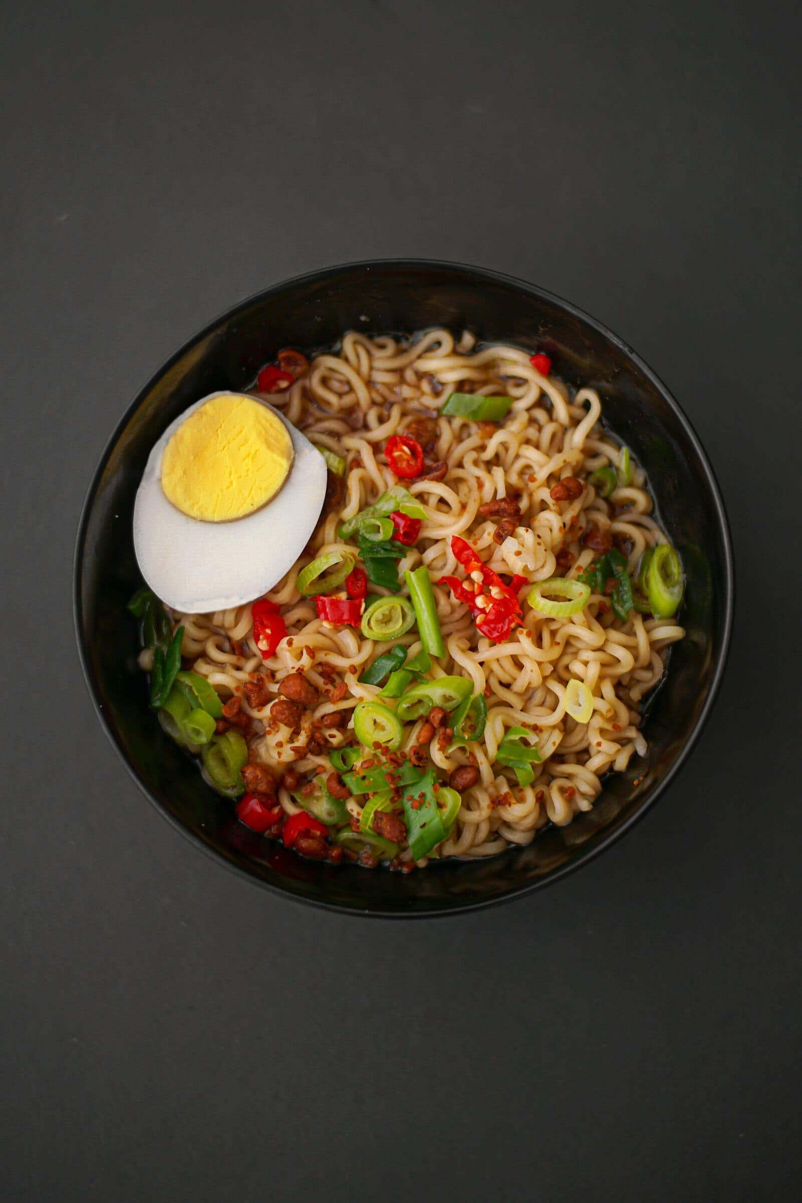 A bowl of instant ramen with a halved egg and chili, seen from above.
