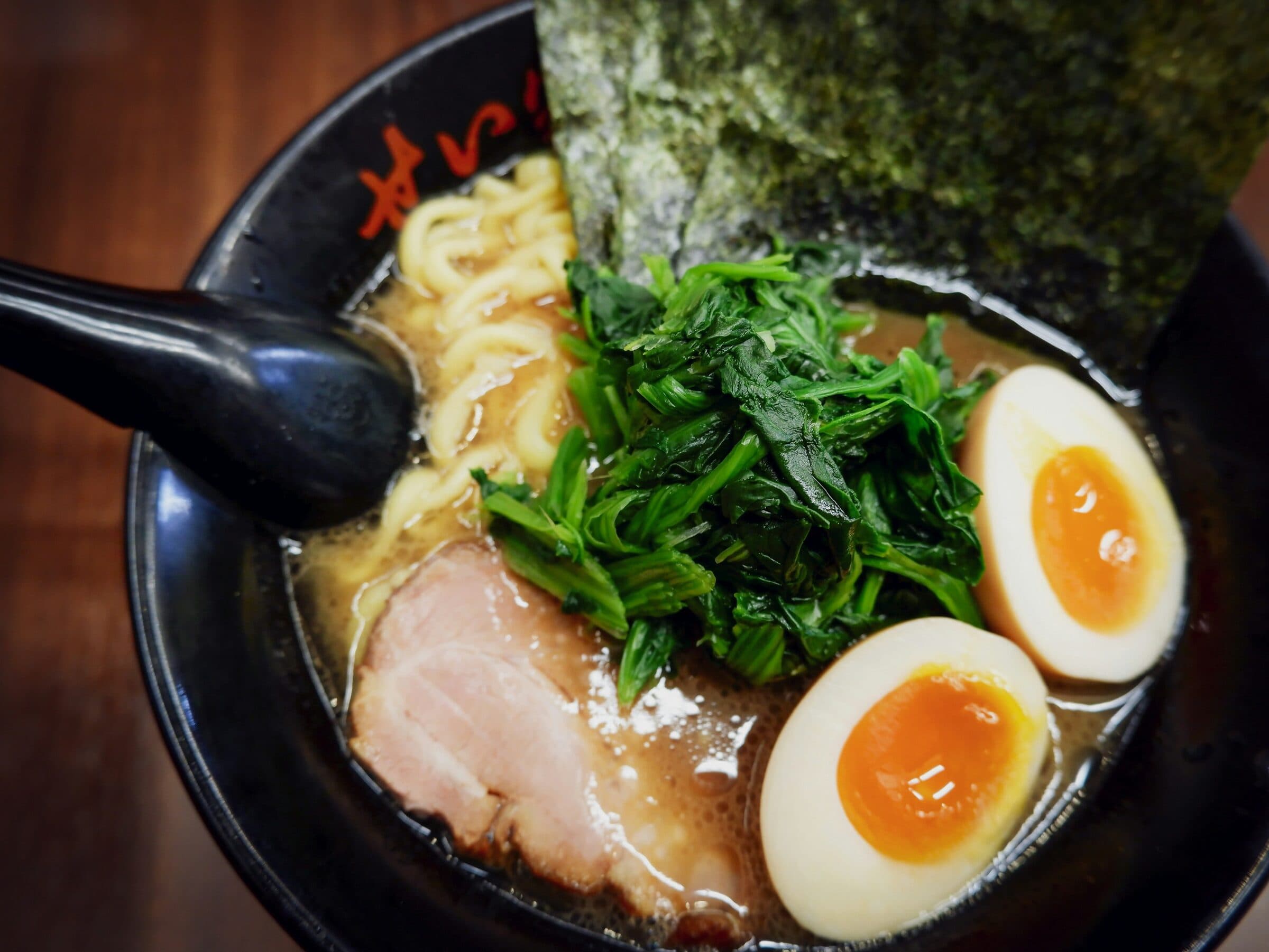 A rich bowl of ramen with chashu, soft eggs, greens and nori.