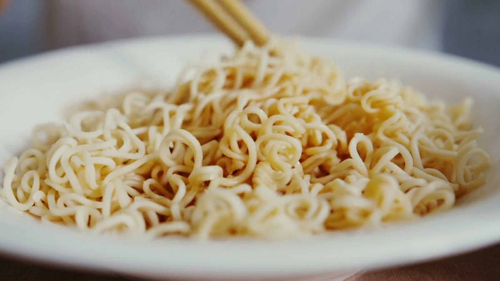 Wavy noodles lifted from a bowl with chopsticks and dropped back in.
