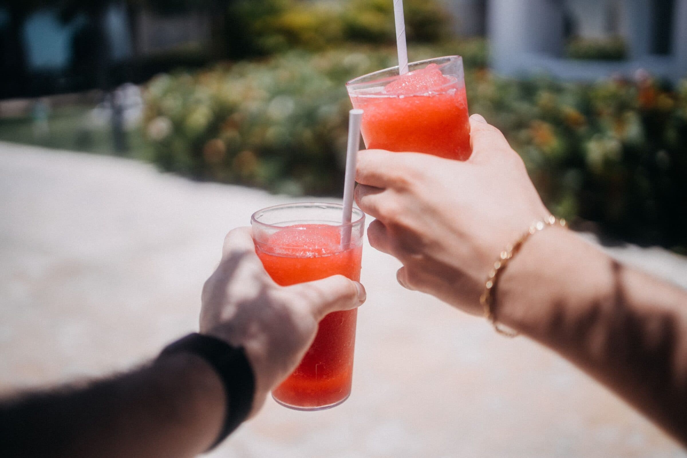 Two friends clink red slushies together on a sunny day.